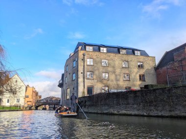 Cambridge, İngiltere - 31 Ocak 2026: Bir grup turist, parlak bir kış gökyüzü altında tarihi tuğla mimarisinin önünden süzülürken Cam Nehri üzerinde geleneksel bir tur yapıyorlar