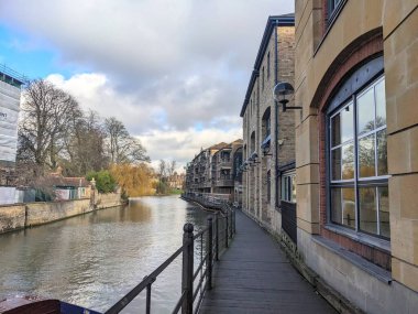 Cambridge, İngiltere - 31 Ocak 2026: Üniversite şehrinin merkezinde bulutlu bir kış gökyüzünün altında tarihi Quayside binalarını ve The River Bar 'ı geçerek nehir kamerasını takip eden bir taş yürüyüş yolu