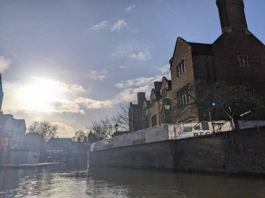 Cambridge, İngiltere - 31 Ocak 2026: Güneş ışığı, parlak bir kış gününde beyaz istifçiliğin arkasında görünen Magdalene Koleji 'nin tarihi tuğla cephesini geçerek Nehir Kamerası' nda parıldıyor