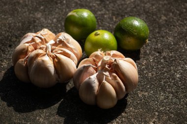 Taze yemek malzemelerinin, sarımsak soğanlarının ve limonların sanatsal durağan hayatı. Koyu kırsal bir zemine karşı çarpıcı güneş ışığıyla aydınlatılıyor.