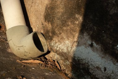 Sert güneş ışığı altında yosunlu beton bir duvara karşı eski bir PVC drenaj borusunu kapatın, kentsel bozulma ve tesisat sorunlarını göstermektedir.