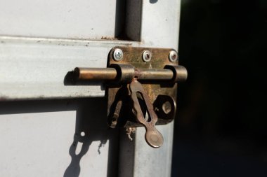 Parlak güneş ışığında paslı bir metal kapı mandalı, güvenliği, zamanı ve eski ev ve donanımın klasik güzelliğini simgeliyor.