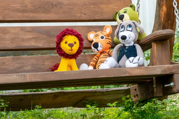 Bir grup amigurumi bebeği sallanan bir bankta oturuyor.