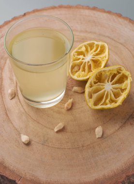 glass of pale yellow citrus juice on a wooden log, squeezed lemon halves and seeds scattered around, fresh homemade beverage and healthy lifestyle concept