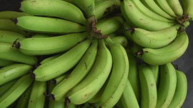 Olgunlaşmamış yeşil muz tarakları, taze çiğ tropikal meyve hasadı, yoğun yeşil muz kümesi, tarım ve sağlıklı yiyecek yığını, 60 fps 'de yavaş çekim.