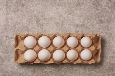 Karton kartondaki on taze beyaz yumurtanın üst görünümü, gri taş arka plan, metin için kopyalama alanı, sağlıklı protein ve kahvaltı konsepti