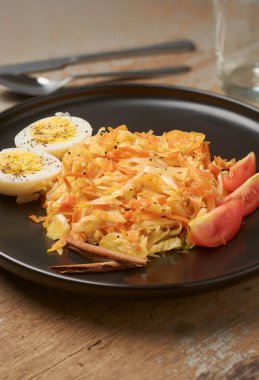 Yakın plan doğranmış havuç ve lahana haşlanmış yumurta, domates dilimleri ve siyah tabakta tarçın çubukları, kırsal ahşap masa arka planı, fotokopi alanı olan sağlıklı yemek kavramı.