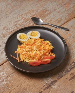 Parçalanmış havuç ve lahana haşlanmış yumurta, domates dilimleri ve siyah tabakta tarçın çubukları, sade ahşap masa arka planı, fotokopi alanı olan sağlıklı yemek kavramı.