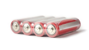 Şeffaf plastik ambalajlı dört kırmızı ve gümüş metal pil izole edilmiş beyaz zemin, parlak filmdeki batarya hücrelerinin metalik terminalleri, yumuşak odaklı yan görüş
