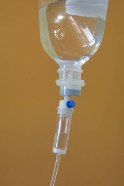 Damardan damlayan bir şişe izole edilmiş bronzlaşmış arka plan, temiz plastik kapta serum ve mavi kapakçık ile tıbbi tüp, yumuşak odak ile yakın kenar görüş, sıvı infüzyonu için damlatma odası