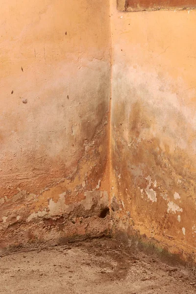Beton zeminde yıpranmış duvar köşesi, nemli yamalı turuncu boya ve küf kalıntıları, fotokopi alanı, yenileme veya endüstriyel grunge arka plan kavramı ile tam çerçeve
