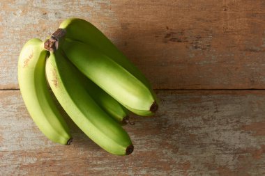 Olgun yeşil muzlar dokuma ahşap masa üzerinde, bir demet pürüzsüz cilt taze meyve, fotokopi alanı ile üst görünüm, taze üretim reklamcılık ve sağlıklı diyet konsepti