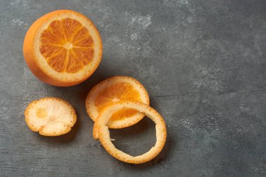 Taze çiğ portakal ve desenli gri masa üzerinde dilimler, narenciye meyvesinin iç sulu ve dairesel kabuk halkaları, yakın çekim, fotokopi alanı ile taze üretim reklam kavramı