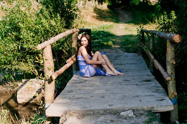 Mujer joven se sienta en el puente de madera — Foto de Stock