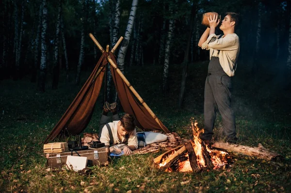 Two twin brothers sitting around a campfire — Stock Photo, Image