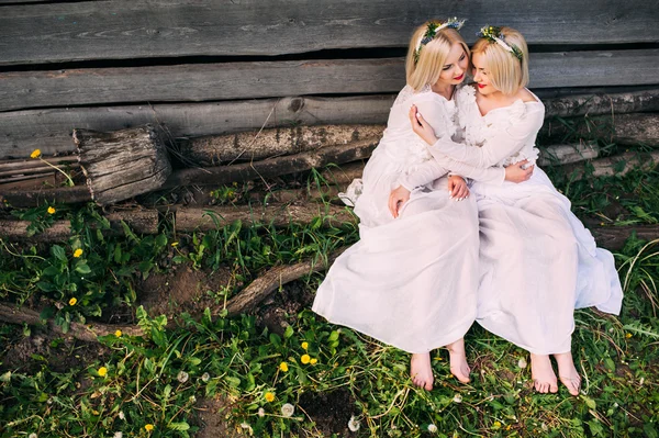 Sestry-dvojčata sedící u dřevěné stěny — Stock fotografie