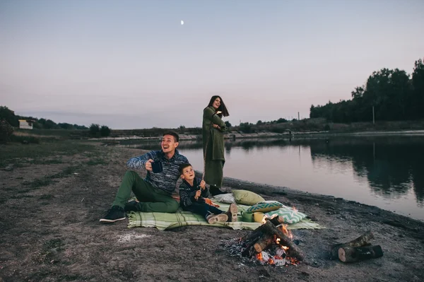 Happy young family sitting around the campfire — Stock Photo, Image