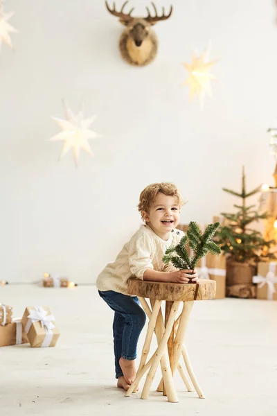 Schöner lockiger kleiner Junge schmückte einen Weihnachtsbaum in einem weißen Raum — Stockfoto