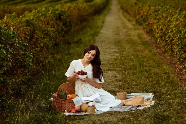 A menina se senta em uma xadrez em um campo perto da fruta. — Fotografia de Stock