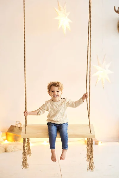 Yakışıklı kıvırcık çocuk Noel ağacını beyaz bir odada süsledi. — Stok fotoğraf
