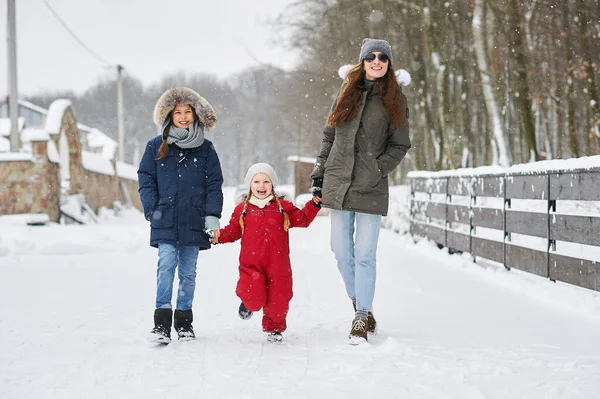 Ein Portret der schönen jungen kaukasischen Mutter mit ihren Kindern im Winter in der Nähe des Hauses mit einem schneebedeckten Weihnachtsbaum im Hintergrund — Stockfoto