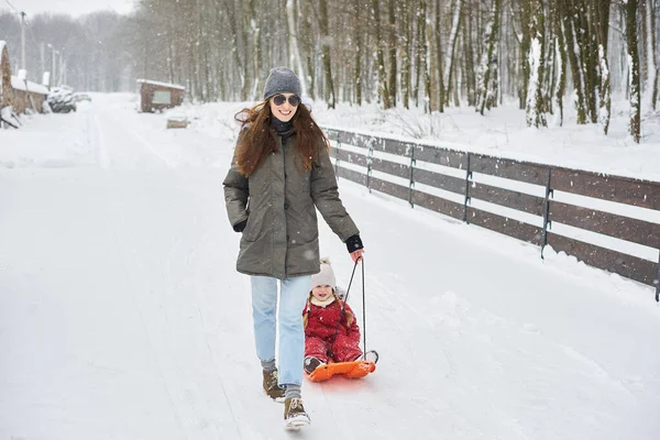 A young beautiful mom sledges her baby — Stock Photo, Image