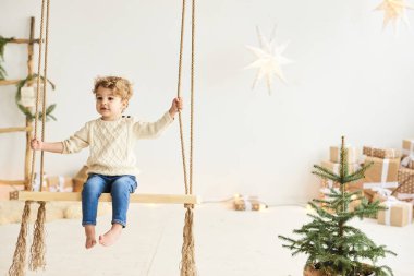 Yakışıklı kıvırcık çocuk Noel ağacını beyaz bir odada süsledi.