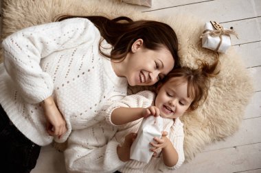 Noel sabahı. Genç ve mutlu bir anne ve kızının yerde yumuşak bir halının üzerinde yatışının en üst görüntüsü. Beyaz kazak giyen kadın ve kız hediyeleri açıyor ve evde birlikte eğleniyorlar..