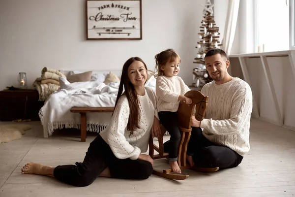 幸せな家族の肖像画 お母さん お父さん 木製のロッキングホースに座っている娘は家でクリスマスを祝うのを楽しんでいます 家族はクリスマスのインテリアの部屋で床に座っています — ストック写真