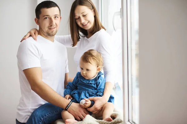 Porträt einer glücklichen jungen Familie mit kleiner Tochter posiert am Fenster in einem hellen Raum. — Stockfoto