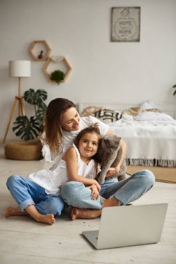 Anne bilgisayar başında çalışırken kız anne ve kediyle oynuyor.