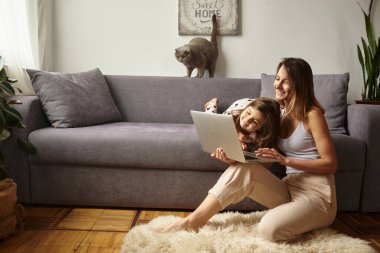 Anne bilgisayar başında çalışırken kız anne ve kediyle oynuyor.