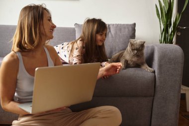Anne bilgisayar başında çalışırken kız anne ve kediyle oynuyor.