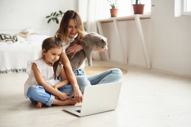 Anne bilgisayar başında çalışırken kız anne ve kediyle oynuyor.