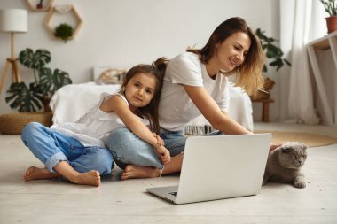 Anne bilgisayar başında çalışırken kız anne ve kediyle oynuyor.