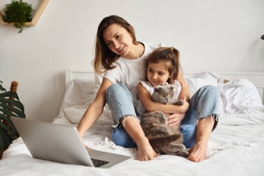 Anne bilgisayar başında çalışırken kız anne ve kediyle oynuyor.