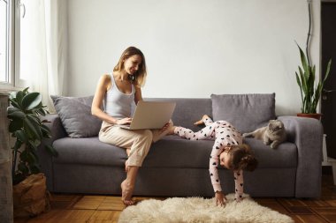 Anne bilgisayar başında çalışırken kız anne ve kediyle oynuyor.