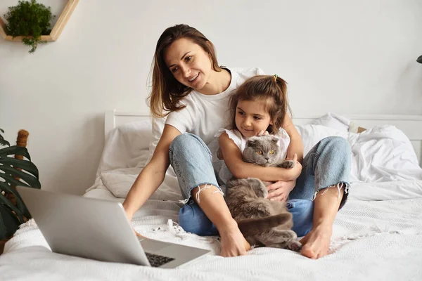 Anne bilgisayar başında çalışırken kız anne ve kediyle oynuyor.