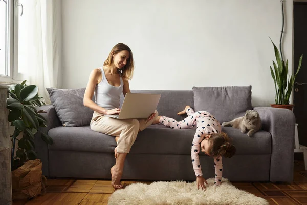 Anne bilgisayar başında çalışırken kız anne ve kediyle oynuyor.