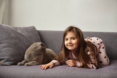 Kız kanepede uzanıyor ve kediyle oynuyor.