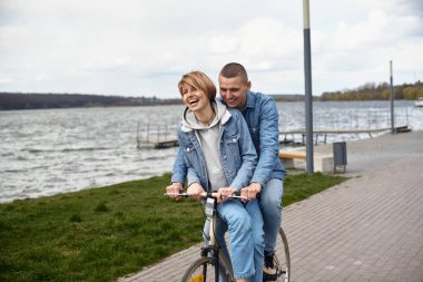 Genç bir çift gölün kenarında bisiklet sürüyor..