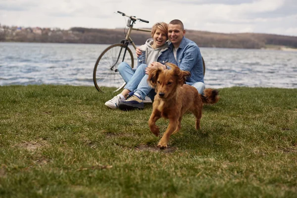年轻夫妇骑自行车在湖边休息 和他们的宠物玩耍 — 图库照片