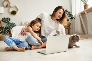 Anne bilgisayar başında çalışırken kız anne ve kediyle oynuyor.