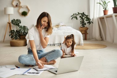 Anne bilgisayar başında çalışırken kız anne ve kediyle oynuyor.