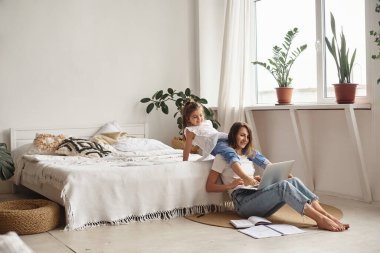 Anne bilgisayar başında çalışırken kız anne ve kediyle oynuyor.