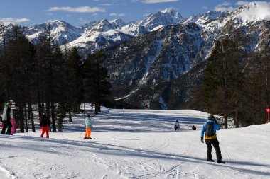 Montgenevre, Fransa - 17 Ocak 2025: Fransız kayak merkezi Montgenevre 'de kayak pistine inen kayakçılar ve snowboardcular. Provence-Alpes-Cte d 'Azur bölgesinde ağaçlı ve karlı kış dağları.