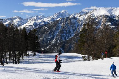 Montgenevre, Fransa - 17 Ocak 2025: Fransız kayak merkezi Montgenevre 'de kayak pistine inen kayakçılar ve snowboardcular. Provence-Alpes-Cte d 'Azur bölgesinde ağaçlı ve karlı kış dağları.