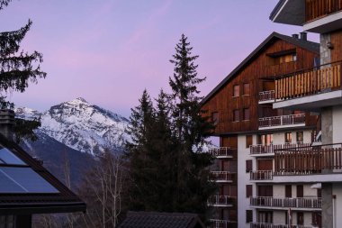 İtalyan alp köyünde ağaçlar ve pastel gökyüzü olan geleneksel ahşap dağ evi. İtalya 'nın karlı dağlarındaki kır evleri. Kayakçılar, kar araçları ve gezginler için bir kış kayak merkezinde konaklama.
