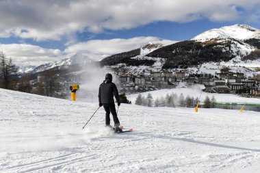 Kayakçılar ve snowboardcular bir İtalyan kayak merkezinde kayak pistine iniyorlar. Piedmont bölgesindeki Sestriere kasabasına bakan geniş karlı bir pistte kayak yapan insanlar. Dağlarda kış tatili