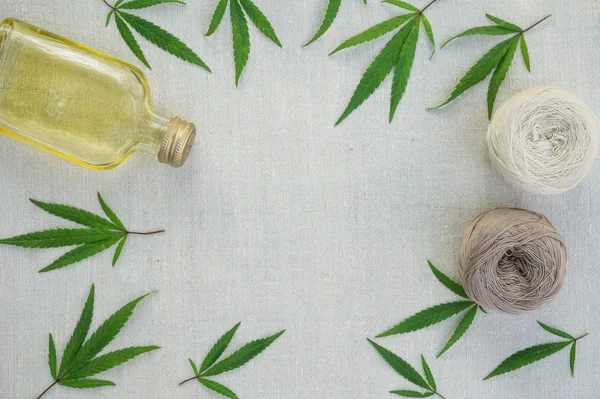 Hojas de cannabis, bolas de hilo y botella de aceite de cáñamo sobre lienzo — Foto de Stock